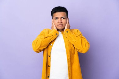 Genç Ekvadorlu adam mor arka planda izole edilmiş hayal kırıklığına uğramış ve kulaklarını kapatmış.