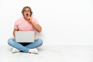 Genç, beyaz arka planda dizüstü bilgisayarı ile yerde oturan beyaz bir adam çözümü bulmak için parmağını kaldırıyor.