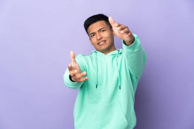 Young Ecuadorian man isolated on purple background presenting and inviting to come with hand