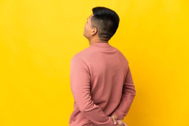 Young Ecuadorian man isolated on yellow background in back position and looking back