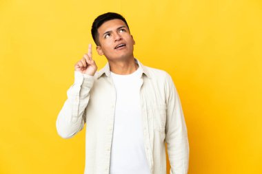Young Ecuadorian man isolated on yellow background thinking an idea pointing the finger up