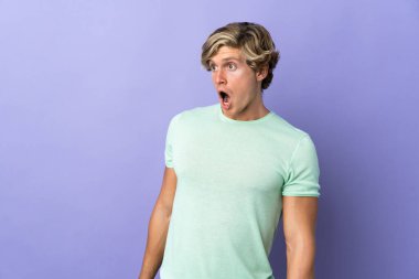 Münzevi mor arka planda İngiliz bir adam yan tarafa bakarken sürpriz jest yapıyor.