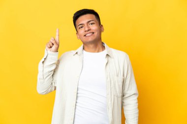Genç Ekvadorlu adam sarı arka planda izole edilmiş. Harika bir fikre işaret ediyor.