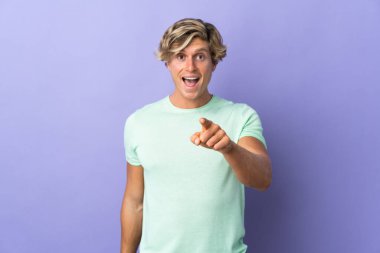 Münzevi mor arka planı olan İngiliz adam şaşırmış ve ön tarafı işaret ediyor.