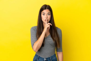 Sarı arka planda izole edilmiş genç Brezilyalı bir kadın sessizlik işareti gösteriyor. Parmağını ağzına sokuyor.