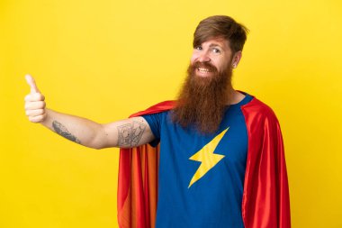 Kızıl saçlı Süper Kahraman sarı arka planda izole edilmiş bir şekilde baş parmak hareketi yapıyor.