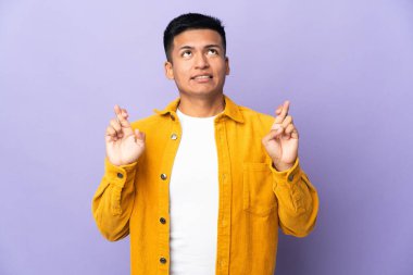 Genç Ekvadorlu adam mor arka planda izole edilmiş, parmakları çapraz ve en iyisini diliyor.