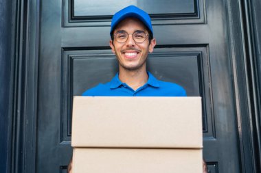 Dışarıdaki teslimatçı çocuk elinde mutlu bir ifadeyle kutuları tutuyor.