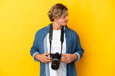 Sarı arka planda izole edilmiş genç fotoğrafçı yan tarafa bakıyor.