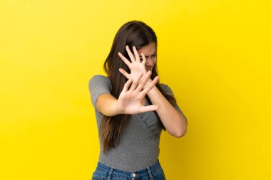 Sarı arka planda izole edilmiş genç Brezilyalı kadın gergin ellerini öne uzatıyor.
