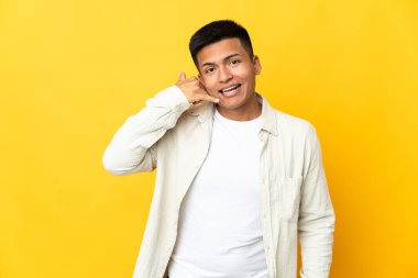 Young Ecuadorian man isolated on yellow background making phone gesture. Call me back sign