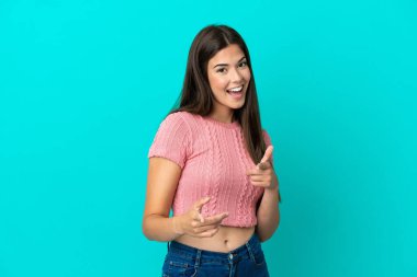 Mavi arka planda izole edilmiş genç Brezilyalı kadın ön tarafı işaret ediyor ve gülümsüyor.