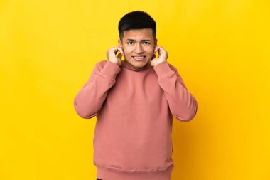 Young Ecuadorian man isolated on yellow background frustrated and covering ears