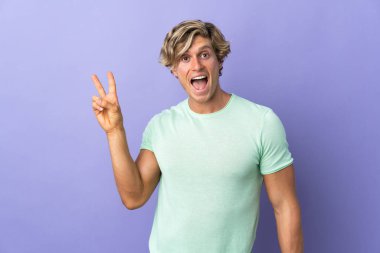 İzole edilmiş mor arka planda gülümseyen ve zafer işareti gösteren bir İngiliz.
