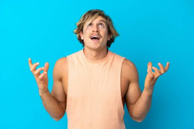 Mavi arka planda izole edilmiş yakışıklı sarışın adam bunalmış.