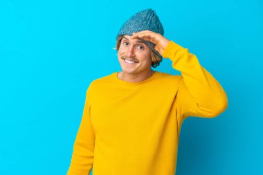 Yakışıklı sarışın adam, mavi arka planda izole edilmiş. Bir şeye bakmak için uzaklara bakıyor.