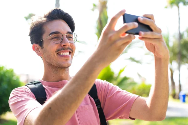 Young Caucasian Man Outdoors Park Using Mobile Phone Doing Selfie — Foto Stock