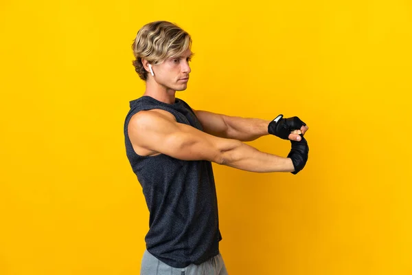 English man over isolated yellow background stretching arm