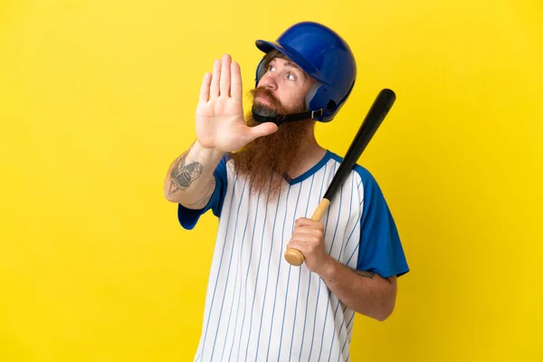 Redhead baseball player man with helmet and bat isolated on yellow background making stop gesture and disappointed