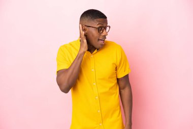 Pembe arka planda izole edilmiş genç latin adam. Kulağına elini sürerek bir şeyler dinliyor.