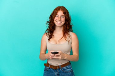 Teenager reddish woman isolated on blue background sending a message with the mobile