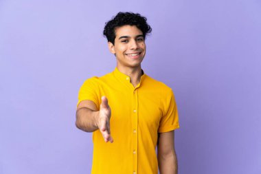 Genç Venezuelalı bir adam mor arka planda izole edilmiş ve iyi bir anlaşma için el sıkışıyor.