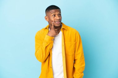 Genç latin adam mavi arka planda izole edilmiş bir şekilde bakarken bir fikir düşünüyor.