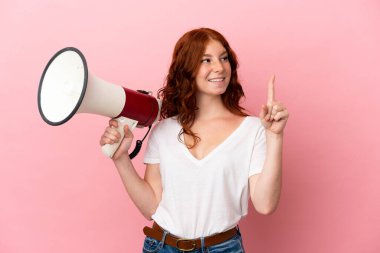 Teenager reddish woman isolated on pink background holding a megaphone and intending to realizes the solution