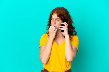 Mavi arka planda izole edilmiş cep telefonu kullanan genç kızılımsı kadının şüpheleri var.