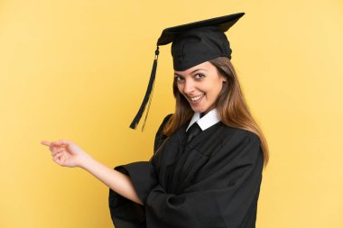 Young university graduate isolated on yellow background pointing finger to the side