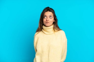 Genç beyaz kadın mavi arka planda izole edilmiş ve yukarı bakıyor.