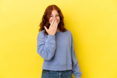Teenager reddish woman isolated on yellow background happy and smiling covering mouth with hand