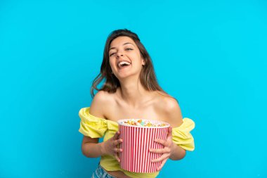 Mavi arka planda izole edilmiş beyaz bir kadın elinde koca bir kova patlamış mısır tutuyor.