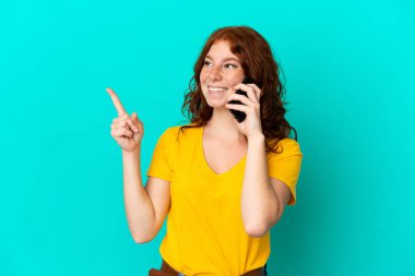 Mavi arka planda izole edilmiş cep telefonu kullanan genç kızılımsı kadın bir parmağını kaldırarak çözümü anlamaya çalışıyor.