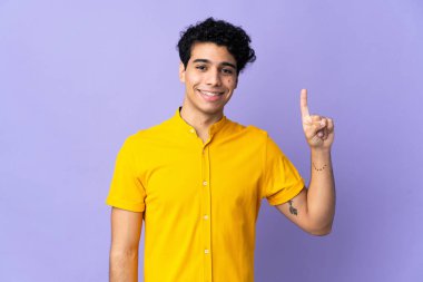 Genç Venezuelalı bir adam mor arka planda izole edilmiş. Harika bir fikre işaret ediyor.