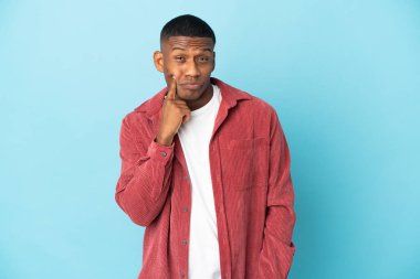 Genç latin adam mavi arka planda izole ve düşünüyor