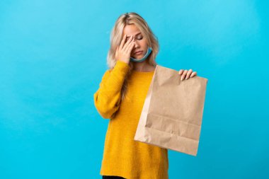Elinde alışveriş torbası tutan genç Rus kadın mavi arka planda başağrısı ile izole edilmiş.