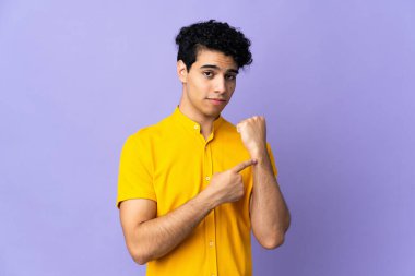 Genç Venezuelalı adam mor arka planda izole edilmiş, geç kalma jesti yapıyor.