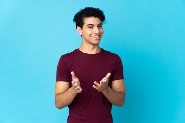 Genç Venezuelalı adam mavi arka planda izole edilmiş bir konferansta sunumdan sonra alkışlıyor.