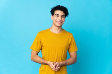Genç Venezuelalı adam mavi arka planda izole edilmiş gülüyor.