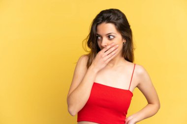 Sarı arka planda izole edilmiş genç beyaz kadın yan tarafa bakarken sürpriz jest yapıyor.