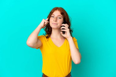Teenager reddish woman using mobile phone isolated on blue background thinking an idea