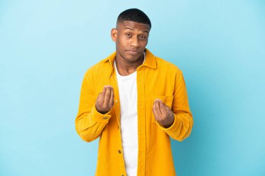 Genç latin adam mavi arka planda izole edilmiş para hareketi yapıyor ama mahvolmuş.