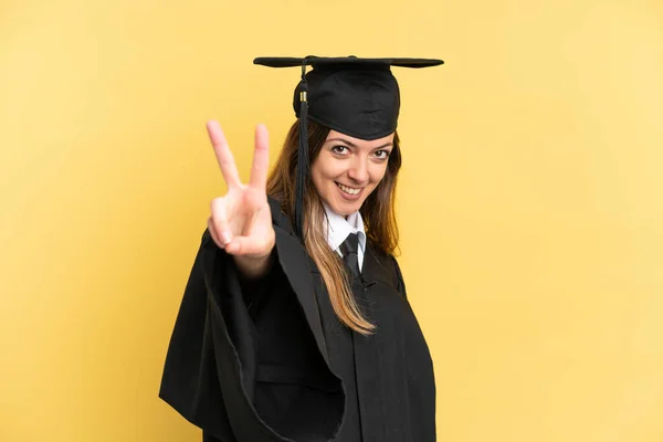 Sarı Arka Planda Izole Edilmiş Genç Üniversite Mezunu Gülümsüyor Zafer — Stok fotoğraf