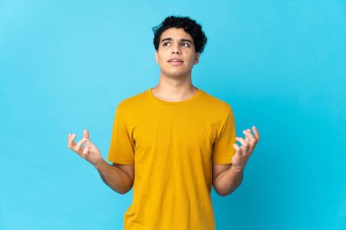 Genç Venezuelalı bir adam mavi arka planda izole edilmiş.