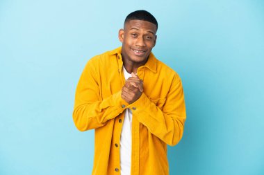 Genç latin adam mavi arka planda yalnız gülüyor.