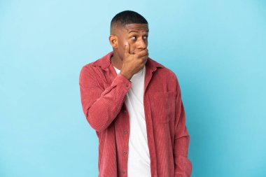 Mavi arka planda izole edilmiş genç latin adam yan tarafa bakarken sürpriz jest yapıyor.