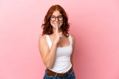Teenager reddish woman isolated on pink background showing a sign of silence gesture putting finger in mouth