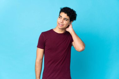 Genç Venezuelalı bir adam mavi arka planda izole edilmiş bir fikir düşünüyor.