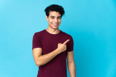 Genç Venezuelalı, mavi arka planda izole edilmiş bir adam bir ürünü sunmak için kenarı işaret ediyor.